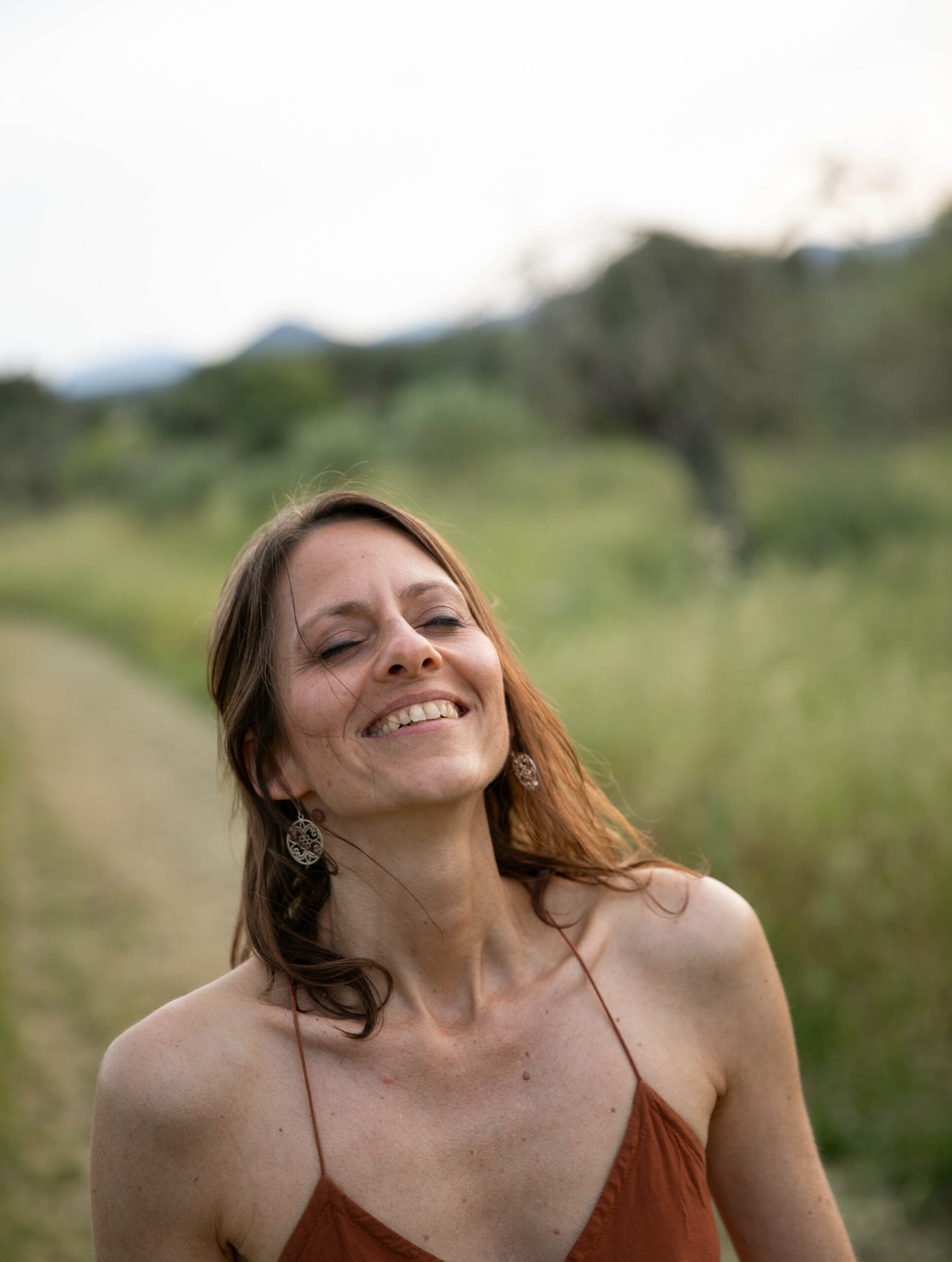 Frau, die einen Waldweg entlangläuft, das gesicht mit geschlossenen Augen in die Sonne streckt und genießt.
